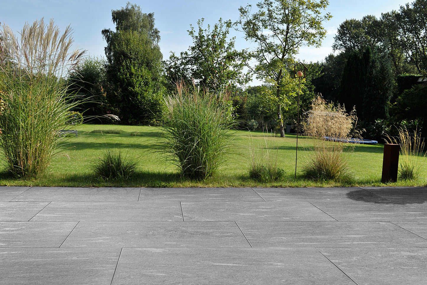 100x50 CeramicLine²-Terrassenplatten in grauer Natursteinoptik von Woehe & Heydemann verlegt auf einer modernen Terrasse mit Blick in den Garten
