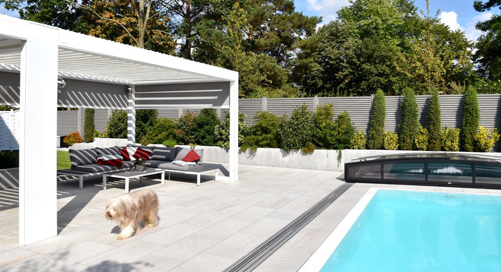100x50 CeramicLine²-Terrassenplatten in beiger Natursteinoptik von Woehe & Heydemann verlegt auf einer modernen Terrasse mit Pool und Hund
