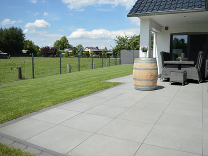 60x60 CeramicLine²-Terrassenplatten in grauer Natursteinoptik von Woehe & Heydemann verlegt auf einer modernen Terrasse mit Fassstehtisch und Sitzecke
