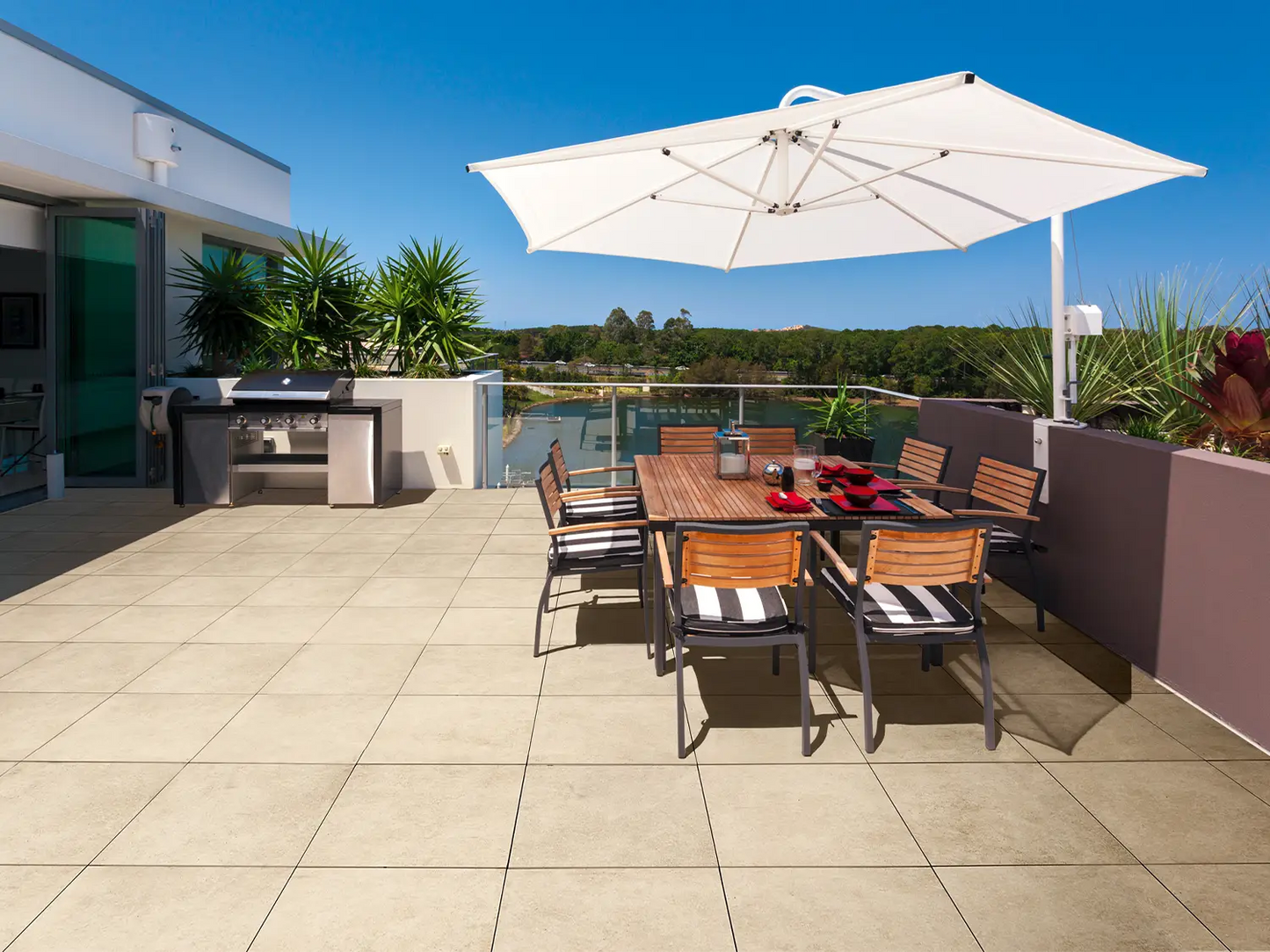 60x60 CeramicLine²-Terrassenplatten in beiger Natursteinoptik von Woehe & Heydemann verlegt auf einer modernen Dachterrasse mit Sonnenschirm und Grill