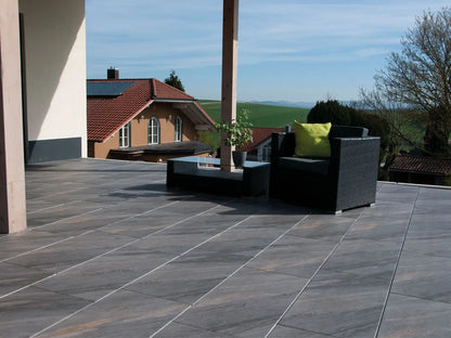 80x40 NanoLine-Terrassenplatten in grauer Natursteinoptik von Woehe & Heydemann verlegt auf einer modernen Terrasse mit Blick auf die Berge