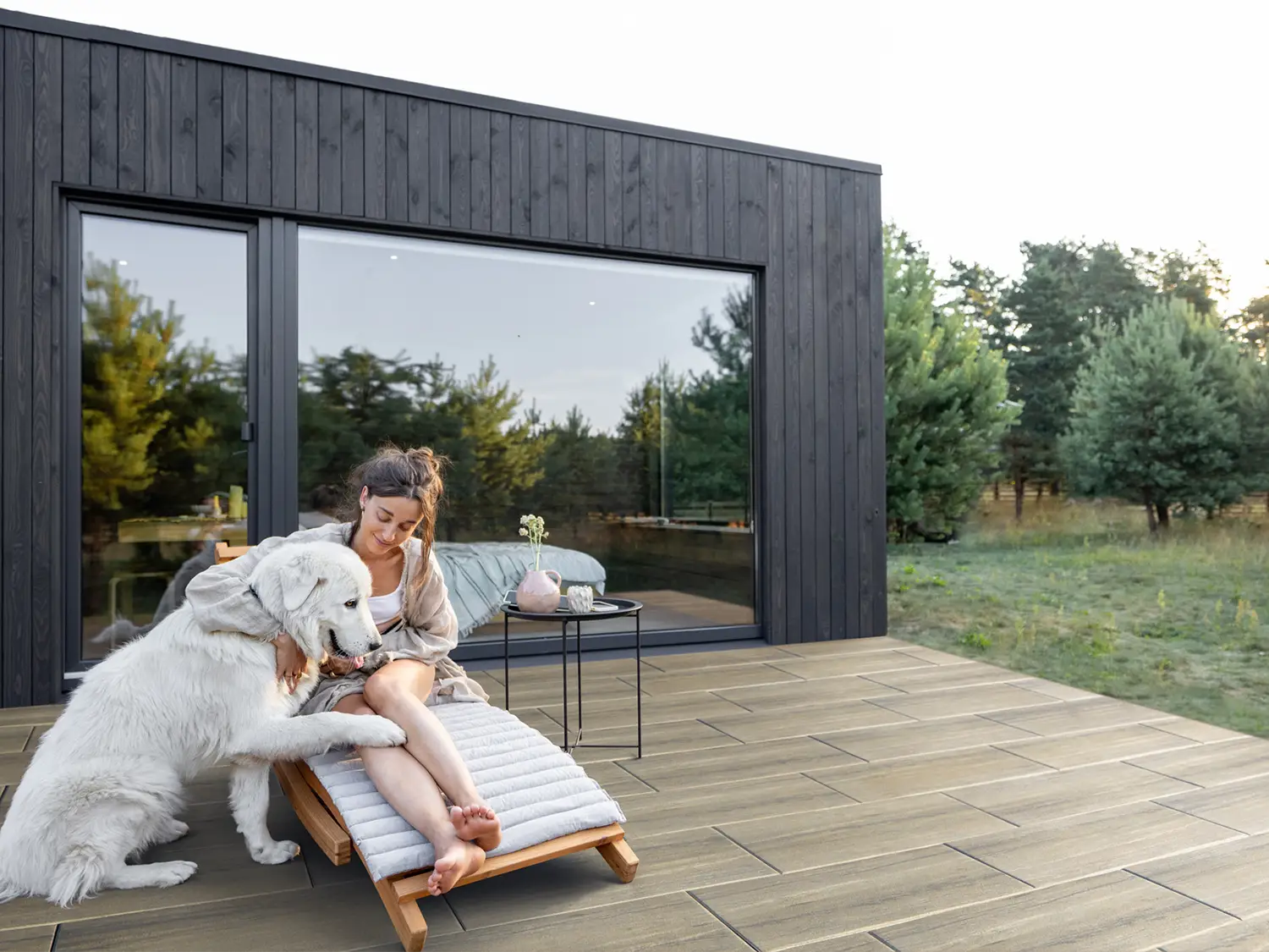 80x40 NanoLine-Terrassenplatten in Holzoptik von Woehe & Heydemann verlegt auf einer modernen Terrasse im Grünen Person mit Hund auf Liegestuhl