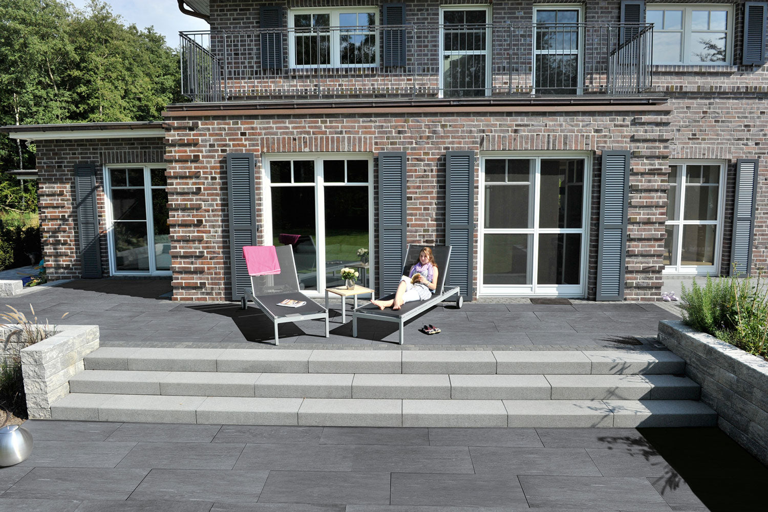 100x50 CreativeLine-Terrassenplatten in grauer Naturstein-Optik von Woehe & Heydemann verlegt auf einer Terrasse mit Liegestühlen und Treppenstufen in den Garten