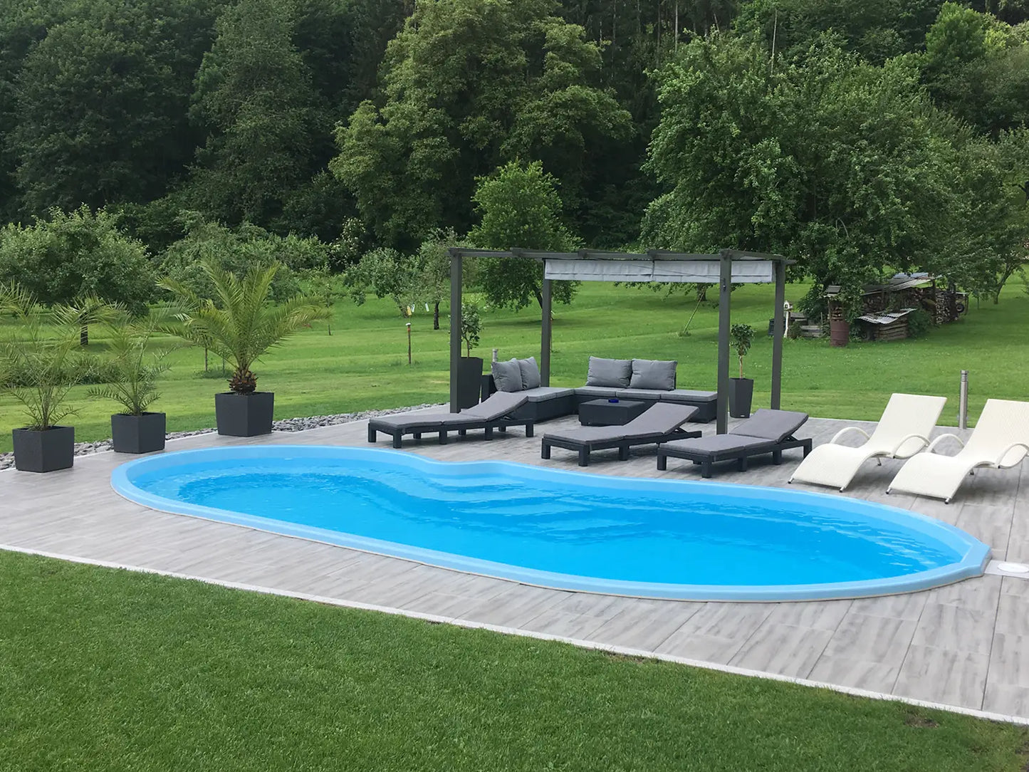 80x40 CreativeLine-Terrassenplatten in grauer Holzoptik von Woehe & Heydemann verlegt auf einer modernen Terrasse im Grünen mit Liegestühlen am Pool