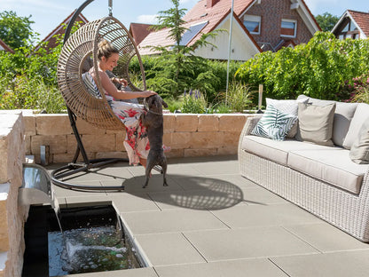 60x40 LuxoGran-Terrassenplatten in beiger Natursteinoptik von Woehe & Heydemann verlegt auf einer Terrasse mit Hängesessel und Wasserspiel