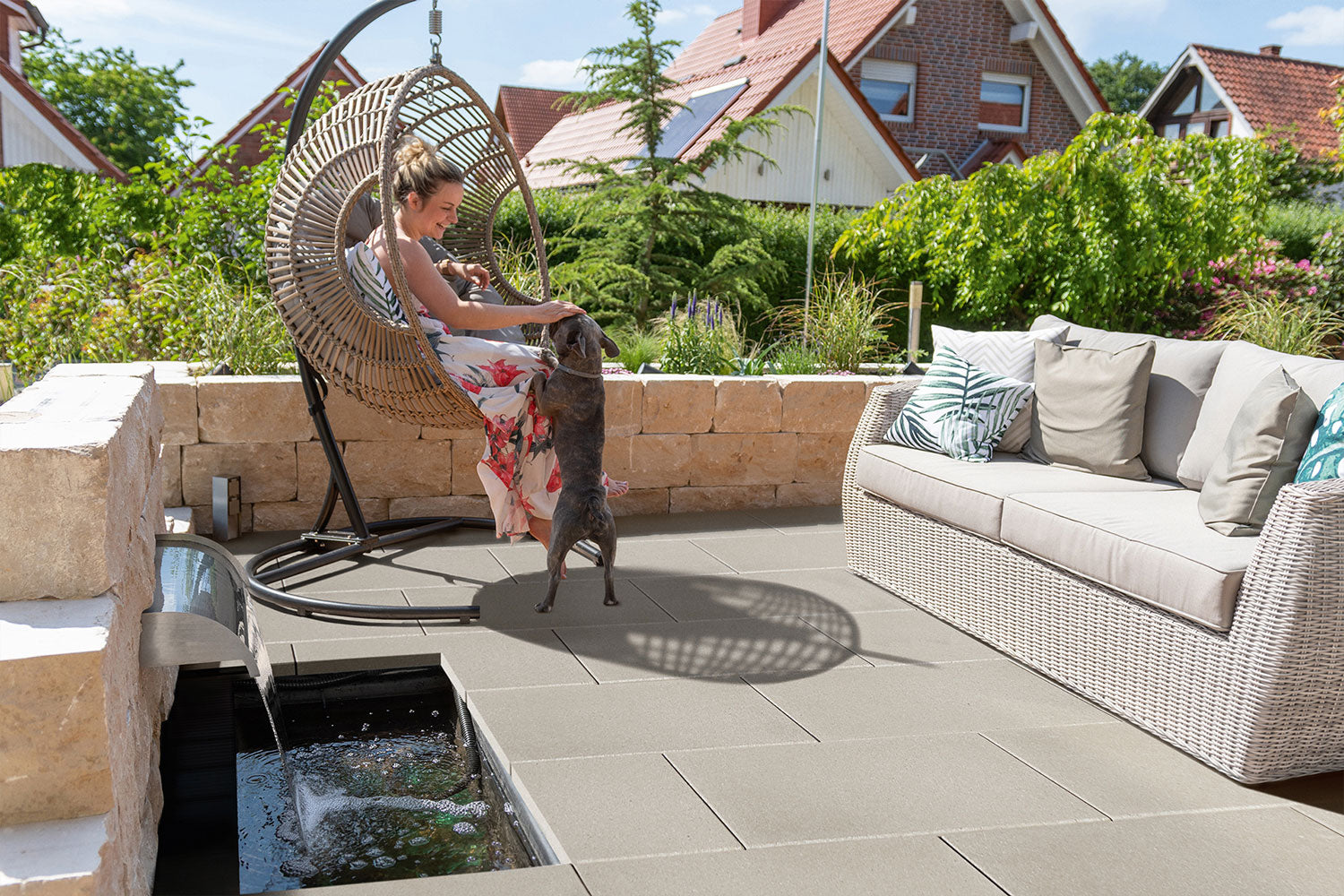 60x40 LuxoGran-Terrassenplatten in beiger Natursteinoptik von Woehe & Heydemann verlegt auf einer Terrasse mit Hängesessel und Wasserspiel