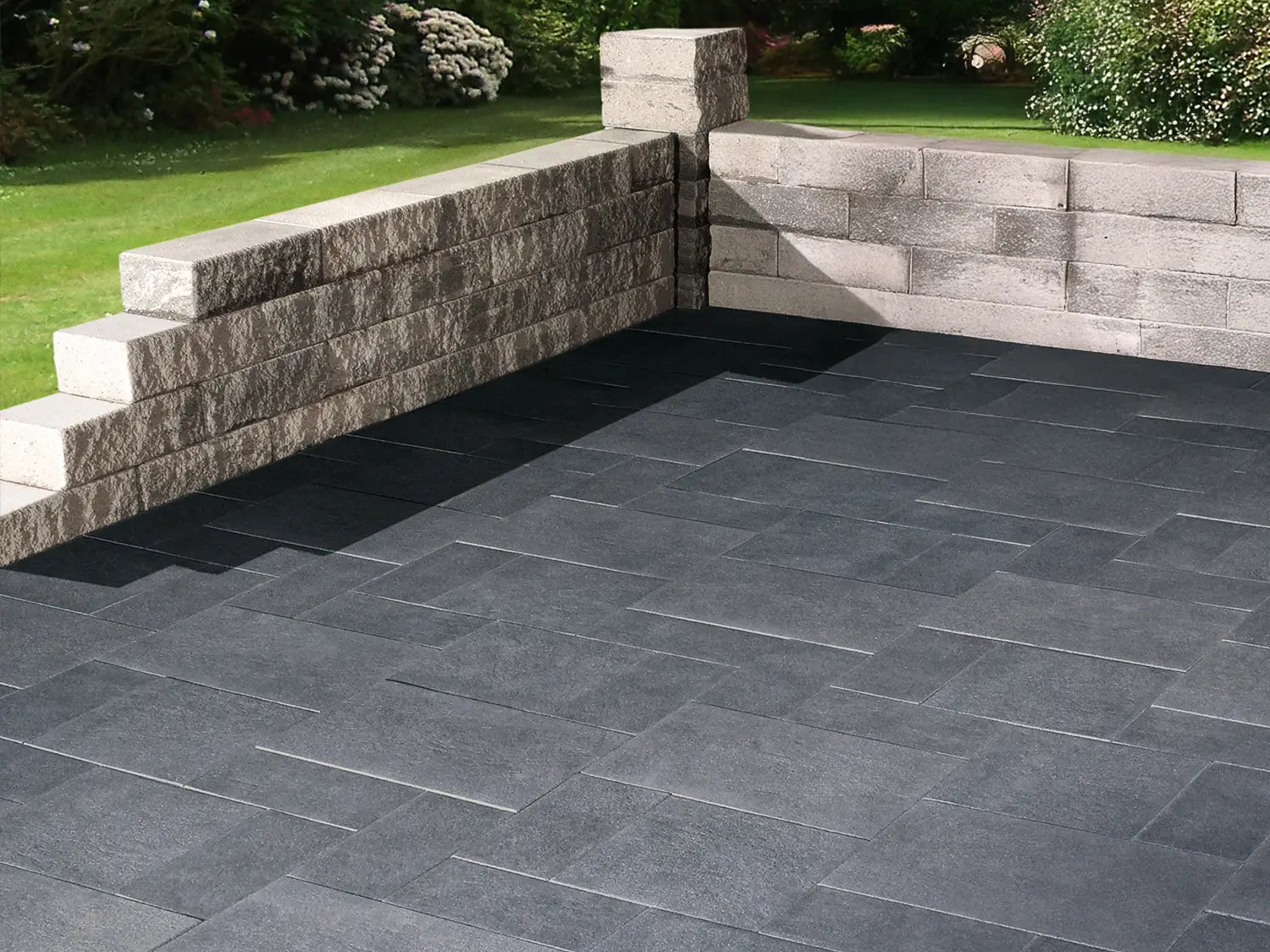NanoLine-Terrassenplatten im Wildverband in grauer Natursteinoptik von Woehe & Heydemann verlegt auf einer modernen Terrasse an einer Mauer 