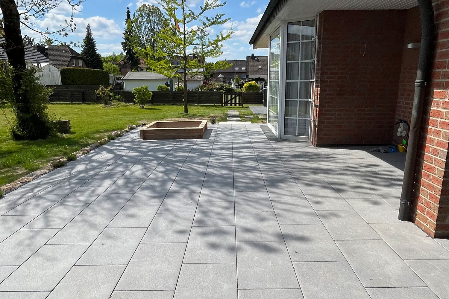 80x40 NanoLine-Terrassenplatten in grauer Natursteinoptik von Woehe & Heydemann verlegt auf einer modernen Terrasse mit Sandkasten
