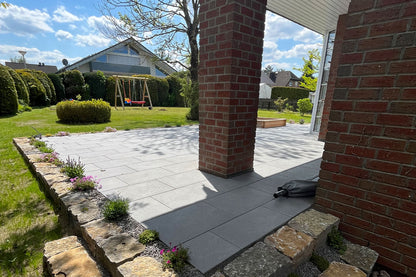 80x40 NanoLine-Terrassenplatten in grauer Natursteinoptik von Woehe & Heydemann verlegt auf einer modernen Terrasse mit Spielgerüst und Blick in den Garten
