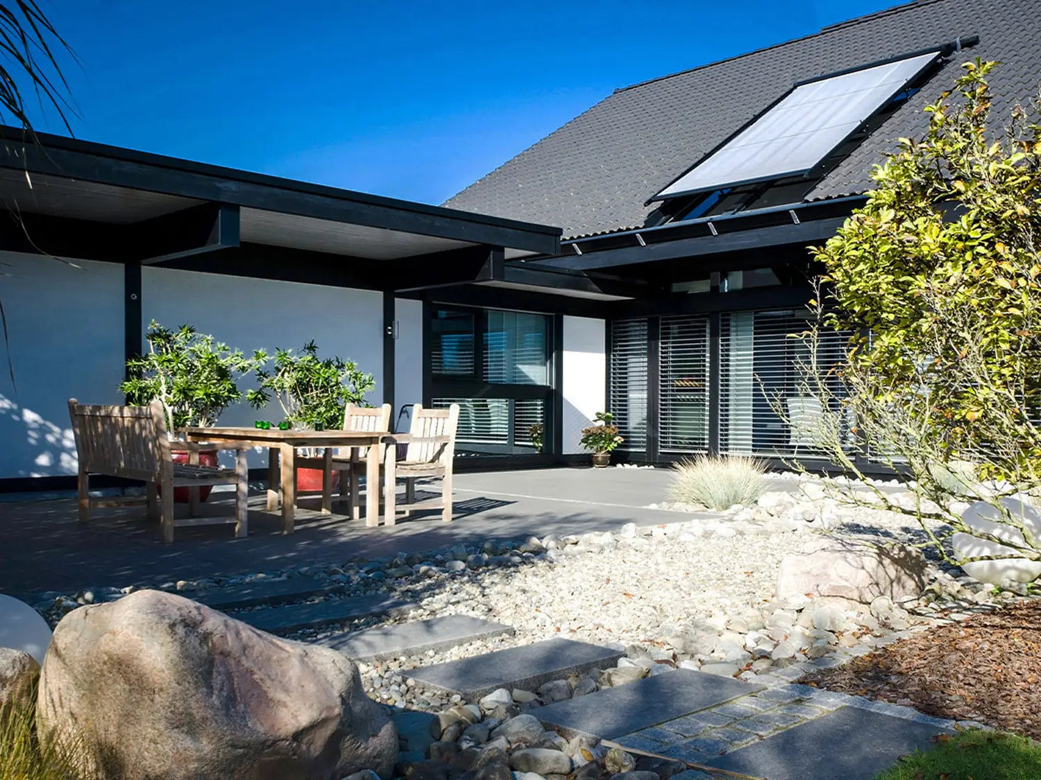 80x40 PremiumLine-Terrassenplatten in grauer Natursteinoptik von Woehe & Heydemann verlegt auf einer modernen Terrasse mit Holzmöbeln und Steingarten