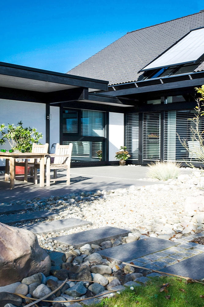 80x40 PremiumLine-Terrassenplatten in grauer Natursteinoptik von Woehe & Heydemann verlegt auf einer modernen Terrasse mit Holzmöbeln und Steingarten