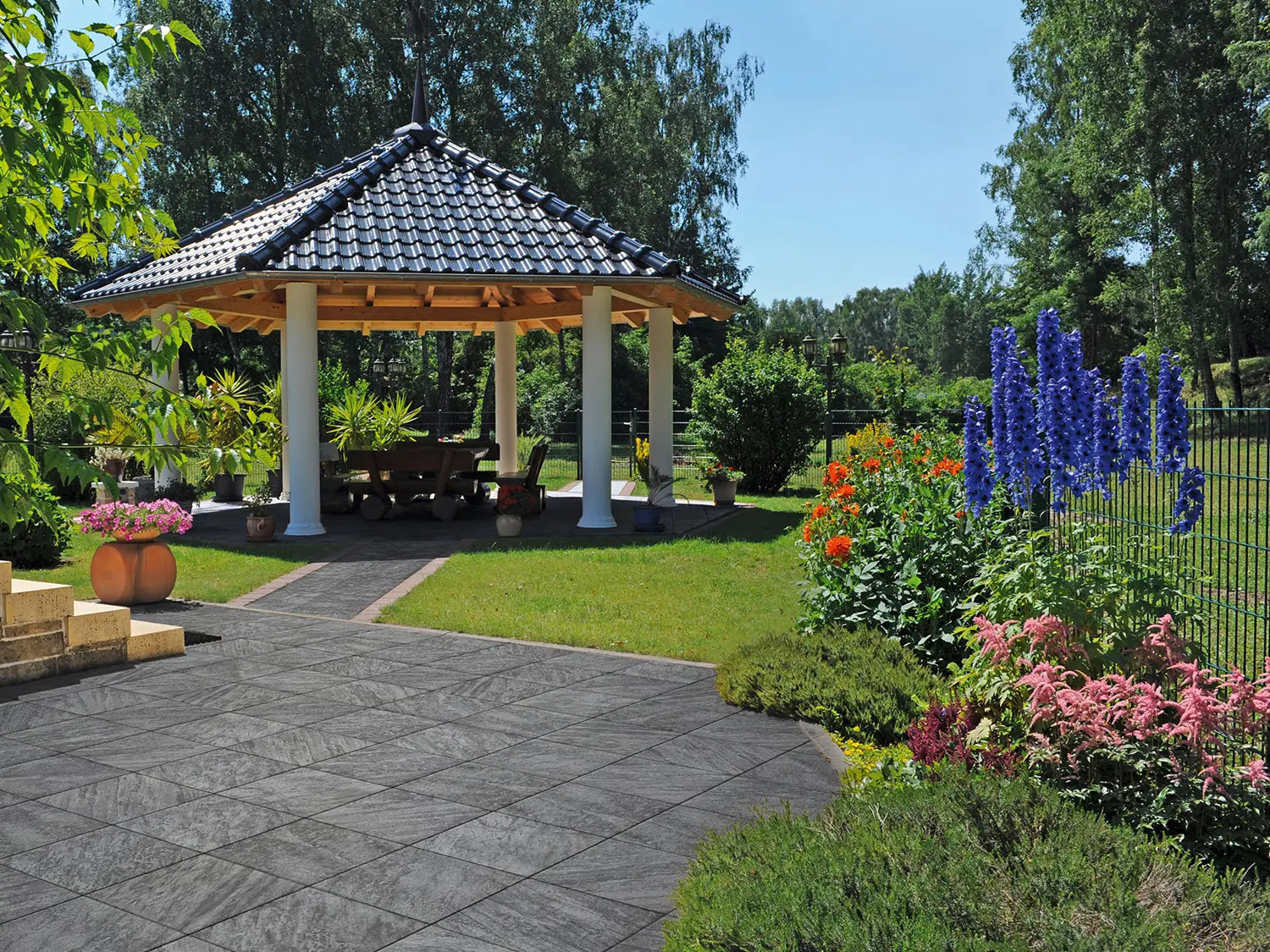 50x50 CreativeLine-Terrassenplatten in grauer Natursteinoptik von Woehe & Heydemann verlegt auf einer modernen Terrasse mit Pavillon und Rasenfläche