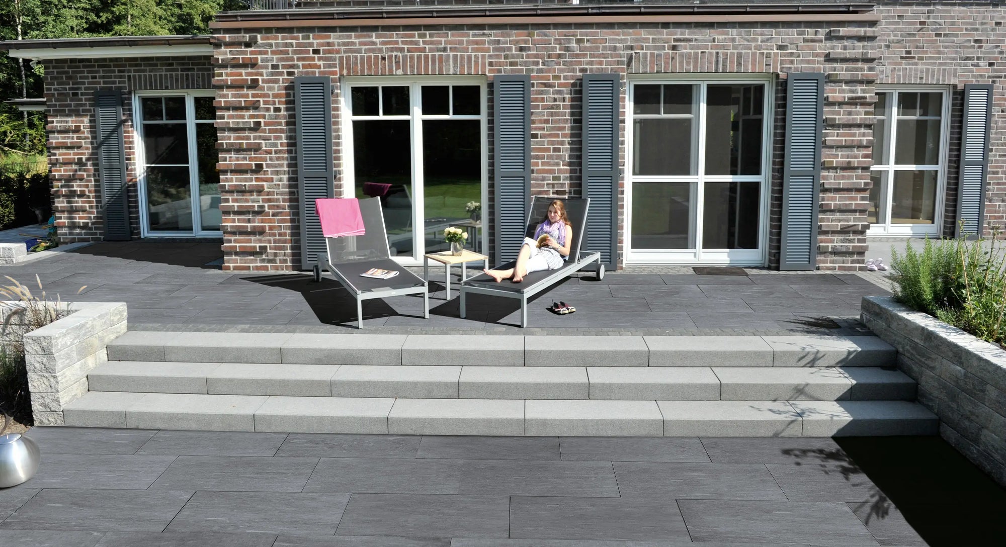 100x50 CreativeLine-Terrassenplatten in grauer Naturstein-Optik von Woehe & Heydemann verlegt auf einer Terrasse mit Liegestühlen und Treppenstufen in den Garten